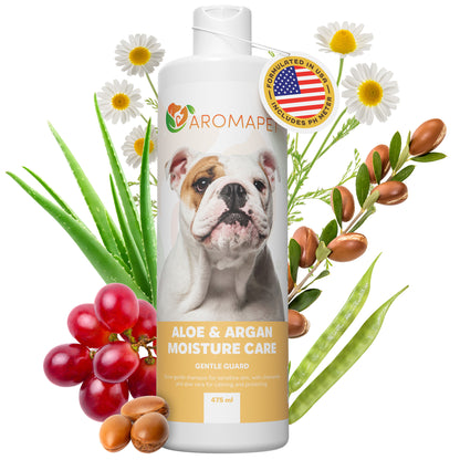 A bottle of Aromaper Aloe & Argan Moisture Care Gentle Guard, featuring a bulldog on the label, surrounded by fresh aloe vera leaves, red grapes, argan nuts, and white daisies on a white background.